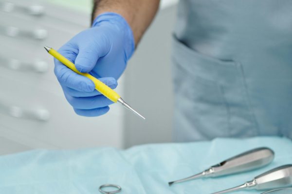 pexels-photo-4269371-4269371 Close-up of a dentist's hand in gloves holding a dental tool over sterilized instruments.
