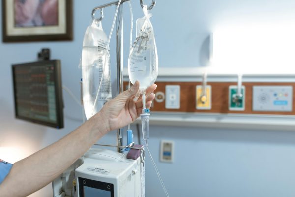 pexels-photo-6129691-6129691 Close-up image of an IV drip and hand in a hospital room, illustrating medical care.