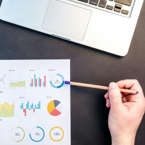 pexels-photo-669621-669621 Hand holding pencil reviewing colorful data charts on desk with laptop.
