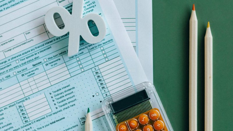 pexels-photo-6863175-6863175 Flat lay of tax documents, calculator, and pencils on green surface.